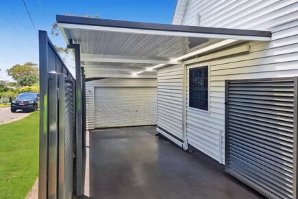 Flat Roof Carports beside white house with secure gate.