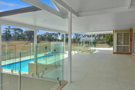 Covered patio with glass fence around pool.