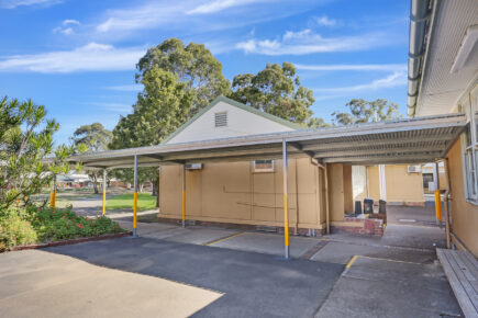 Covered school walkway with garden and trees.