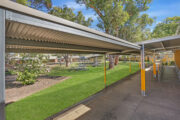 Covered walkway in school courtyard with green grass.